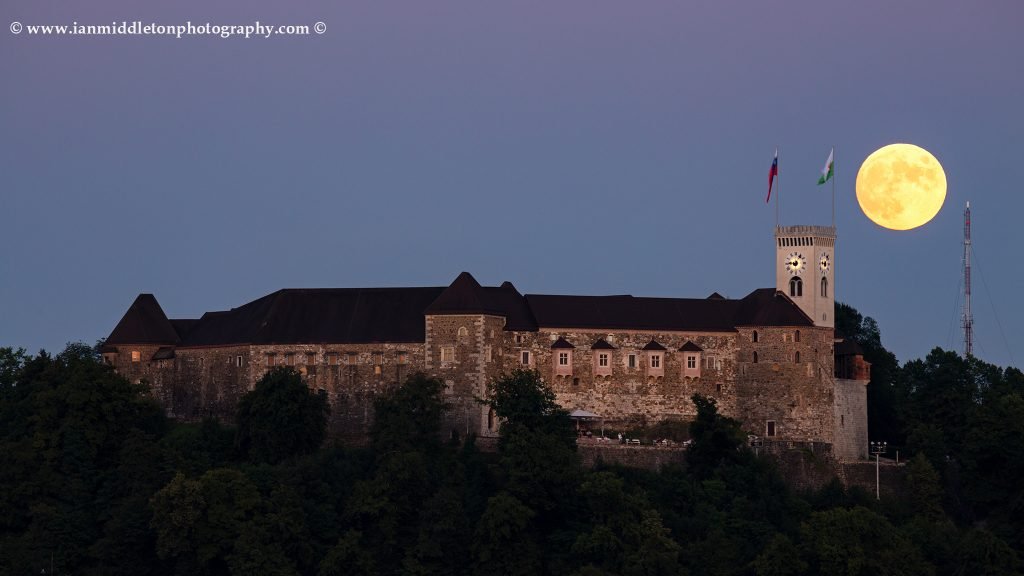 View across the to Ljubljana Castle as the full moon rises behind the tower. Seen from Tivoli Park, Ljubljana, Slovenia.